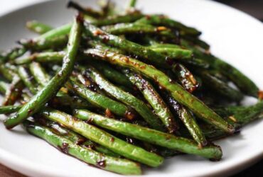 A close-up serving of vibrant green beans coated in a glossy, dark garlic sauce, ready to eat.