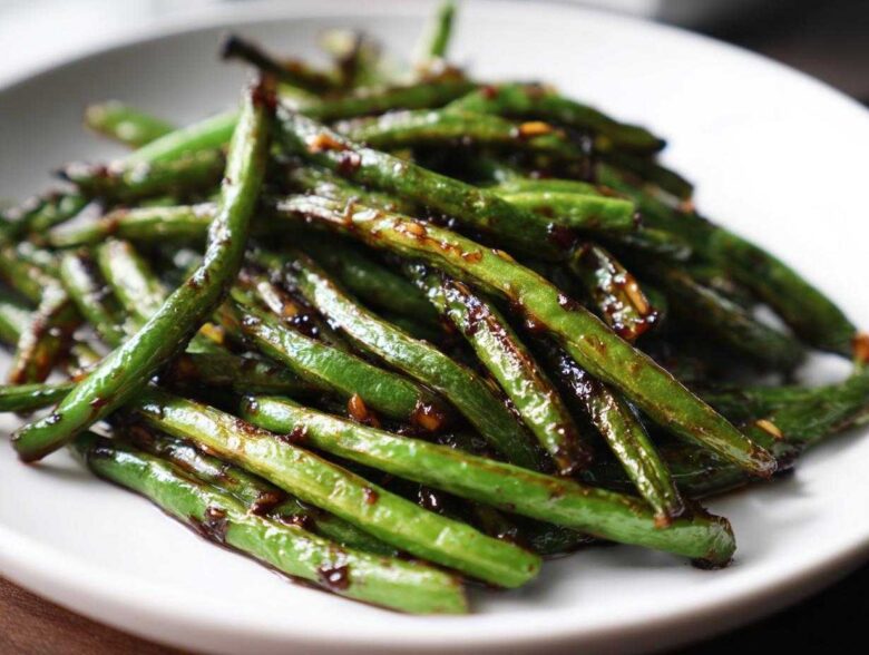 A close-up serving of vibrant green beans coated in a glossy, dark garlic sauce, ready to eat.