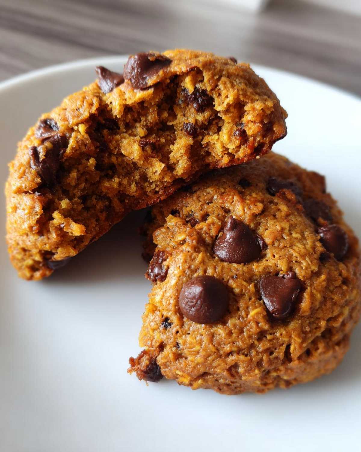 A rich, orange-toned chocolate chip breakfast cookie broken in half, showing its soft, moist interior.