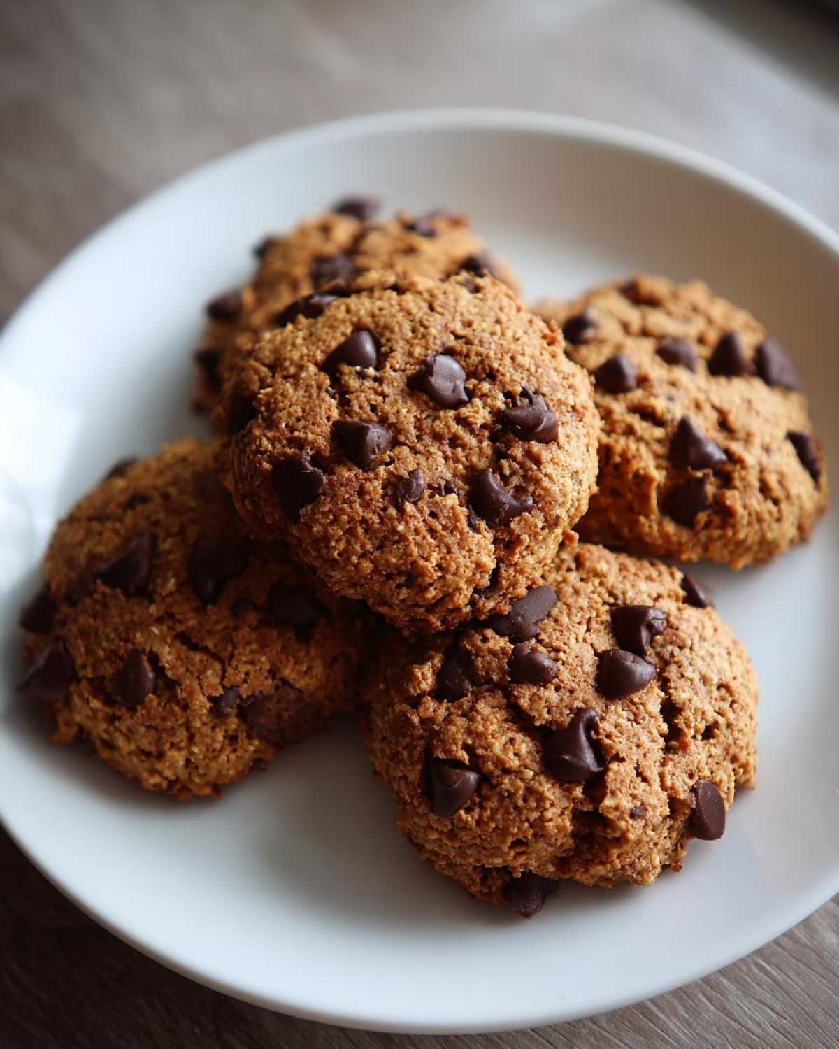 A stack of four textured, golden-brown breakfast cookie treats loaded with chocolate chips on a white plate.