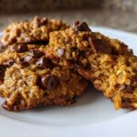 Close-up of several moist, golden-brown breakfast cookie treats loaded with melted chocolate chips on a white plate.