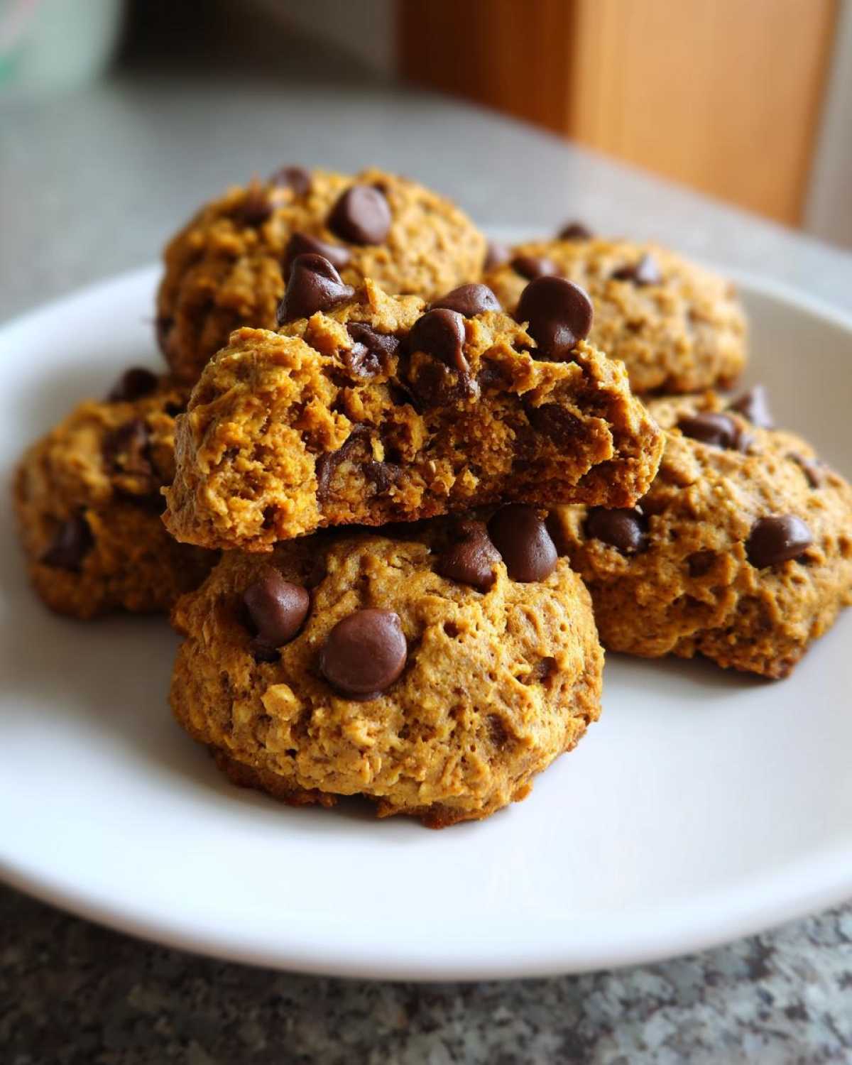 A stack of moist, pumpkin-colored breakfast cookie halves filled with chocolate chips, one cookie broken open.
