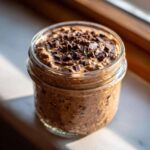 Close-up of creamy chocolate overnight oats in a glass jar, topped generously with dark chocolate shavings.