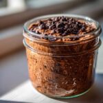 A close-up of rich chocolate overnight oats topped with mini chocolate chips in a clear glass jar.