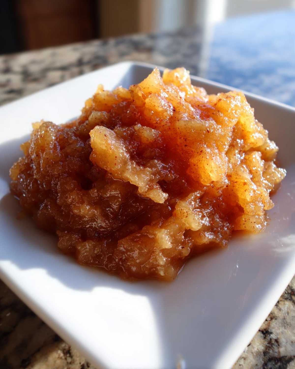 Close-up of chunky, homemade applesauce seasoned with cinnamon, served on a small white square dish.
