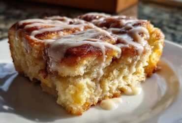 A close-up, sunlit shot of a gooey slice of Cinnamon roll casserole topped with thick white icing.