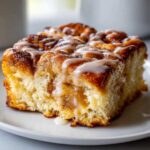 Close-up of a fluffy slice of cinnamon roll casserole drizzled generously with white vanilla icing.