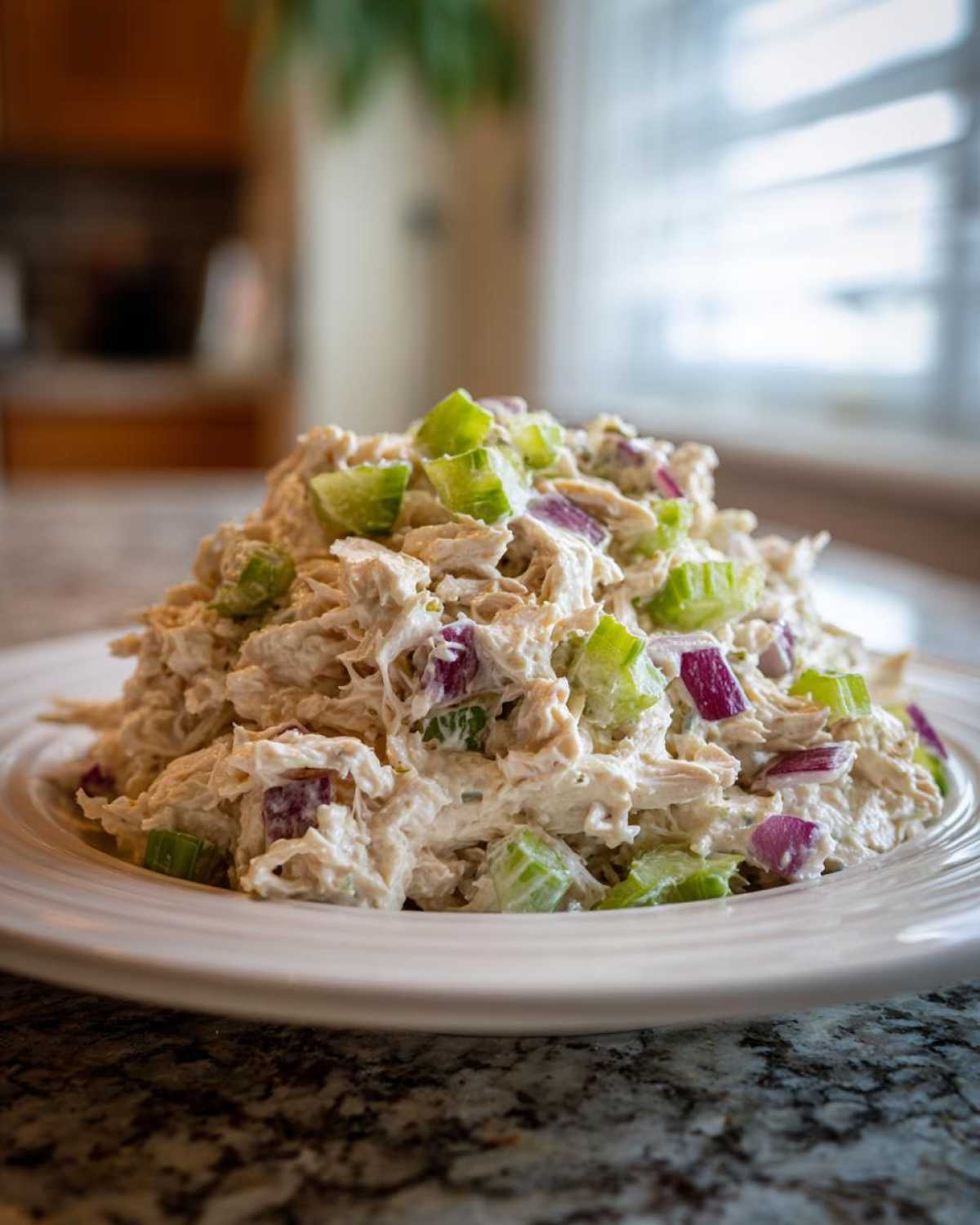 A close-up of a generous serving of cottage cheese chicken salad mixed with chopped celery and red onion on a white plate.