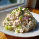 A mound of creamy cottage cheese chicken salad mixed with diced celery and red onion, garnished with herbs.
