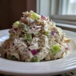 A mound of creamy cottage cheese chicken salad mixed with bright green celery and purple red onion chunks, served on a white plate.