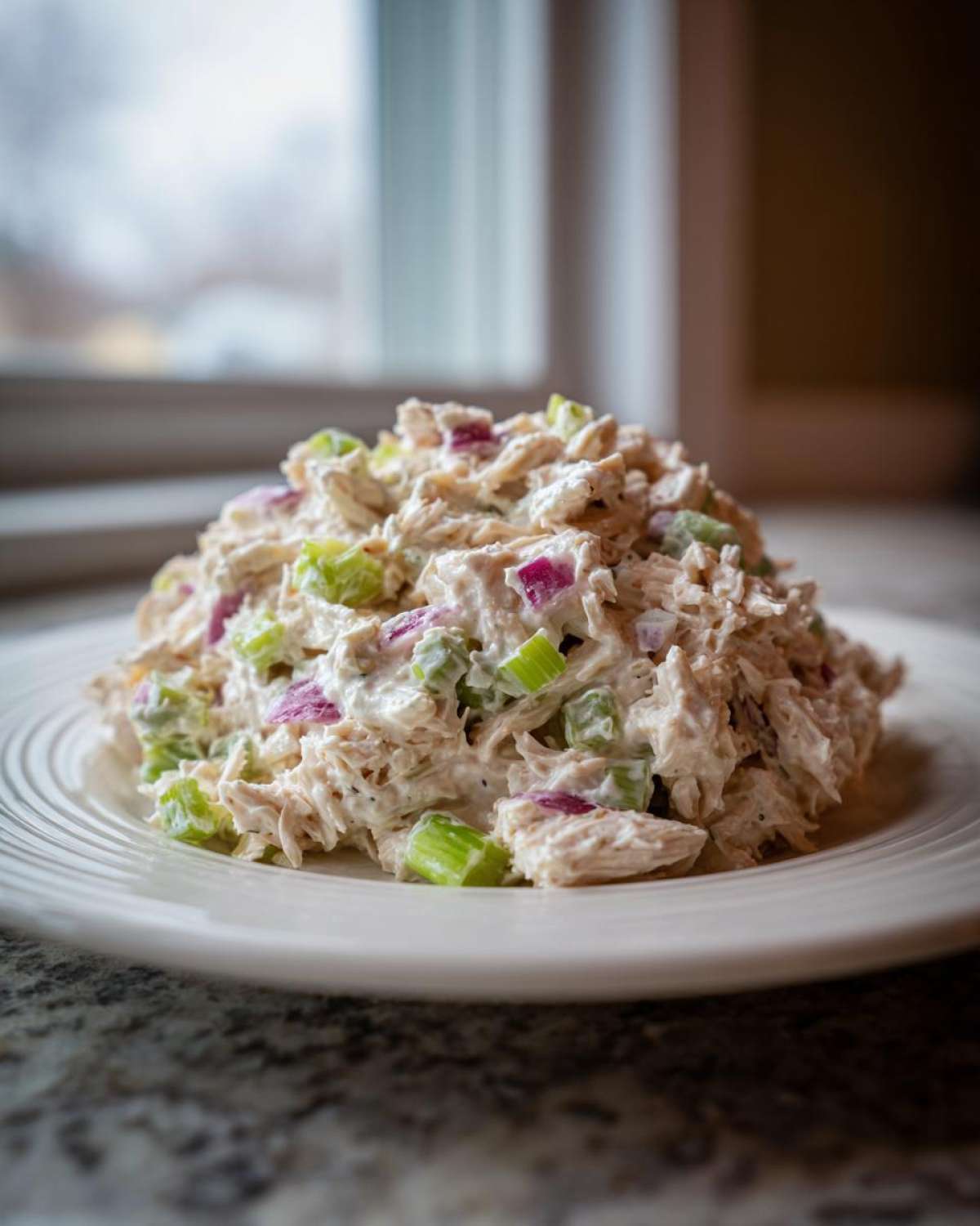 A mound of creamy cottage cheese chicken salad mixed with diced celery and red onion served on a white plate.