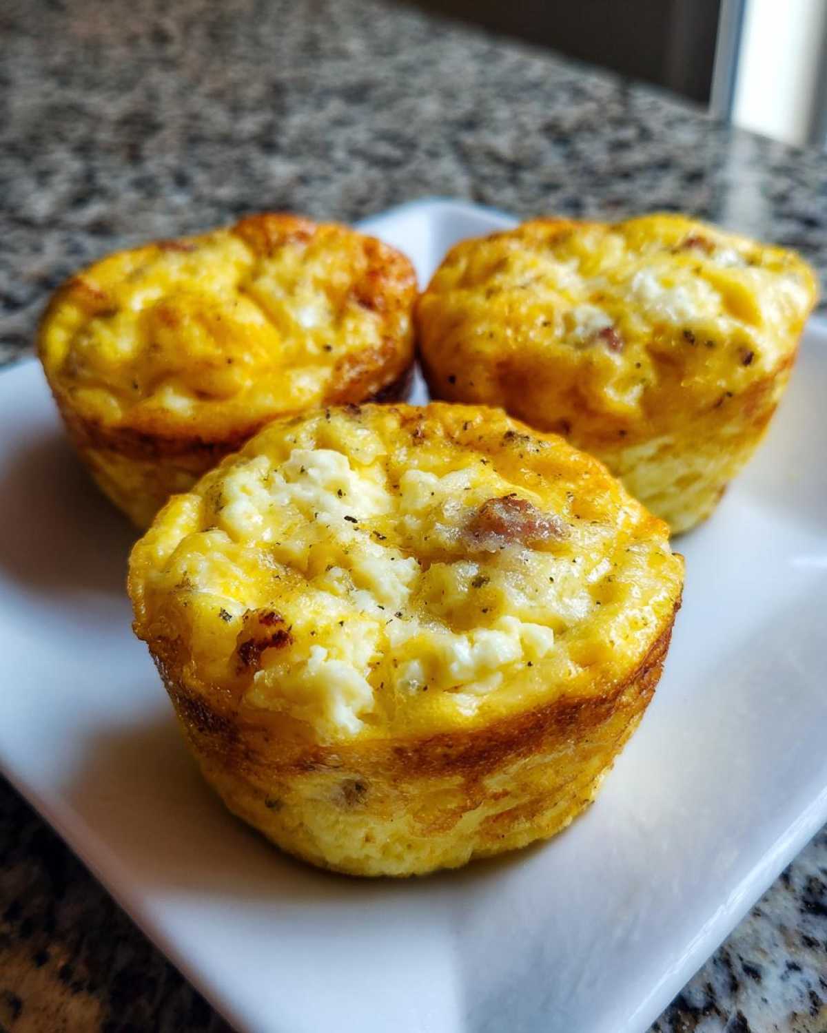 Three golden-brown cottage cheese egg cups, featuring visible cottage cheese curds, served on a small white plate.