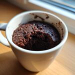 A rich, dark Cottage Cheese Microwave Brownie baked inside a white mug, topped with chocolate chips.