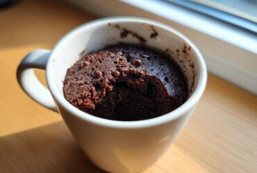 A rich, dark Cottage Cheese Microwave Brownie baked inside a white mug, topped with chocolate chips.