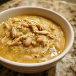 Close-up of a white bowl filled with creamy crockpot white chicken chili, showing shredded chicken and white beans.
