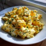 A close-up of creamy egg salad recipe chunks mixed with mayonnaise and topped generously with chopped green herbs.