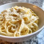 Close-up of fettuccine pasta coated in creamy homemade alfredo sauce, topped with grated Parmesan and black pepper.