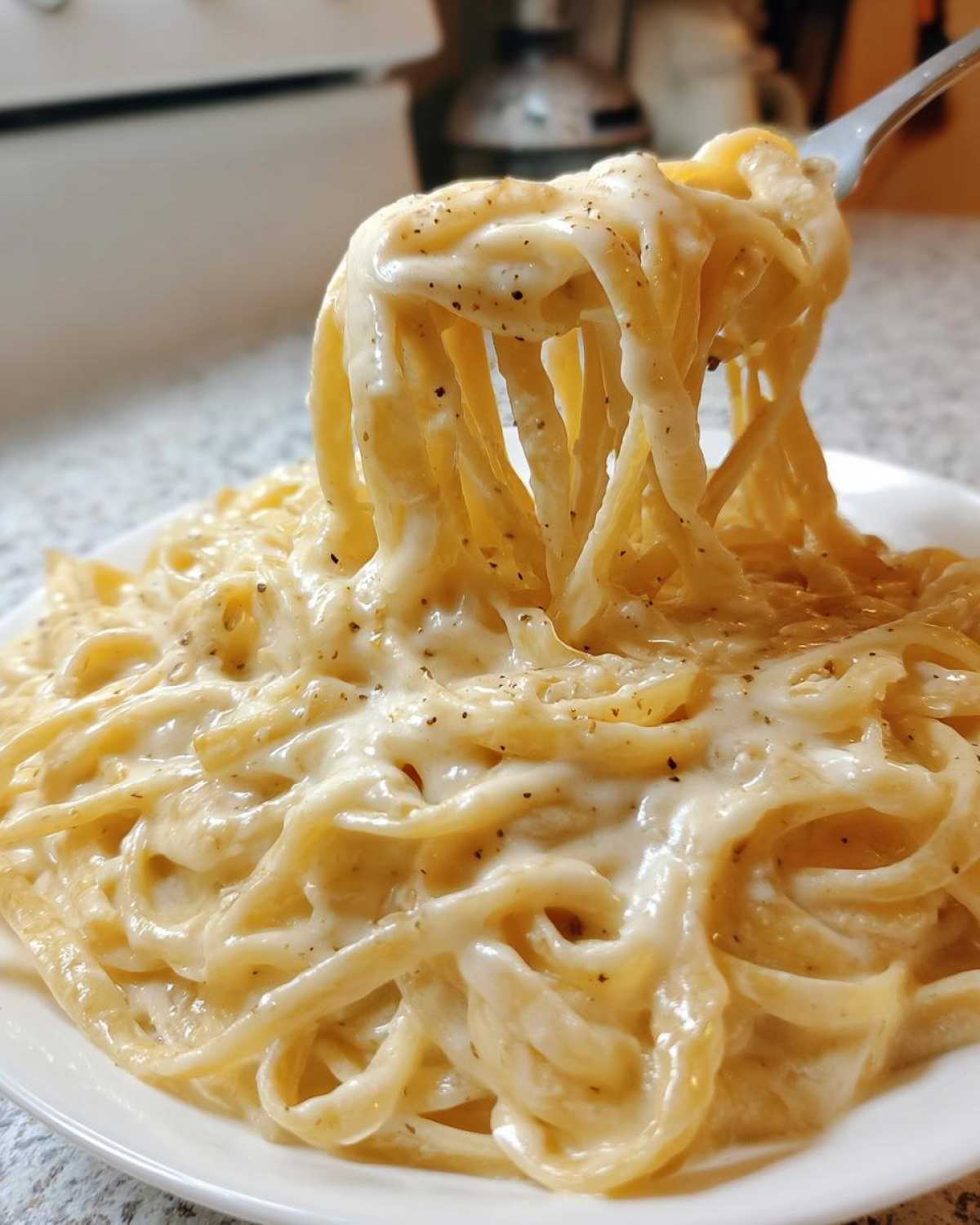 A fork lifting creamy fettuccine noodles coated thickly in rich Olive Garden Alfredo Sauce, speckled with black pepper.