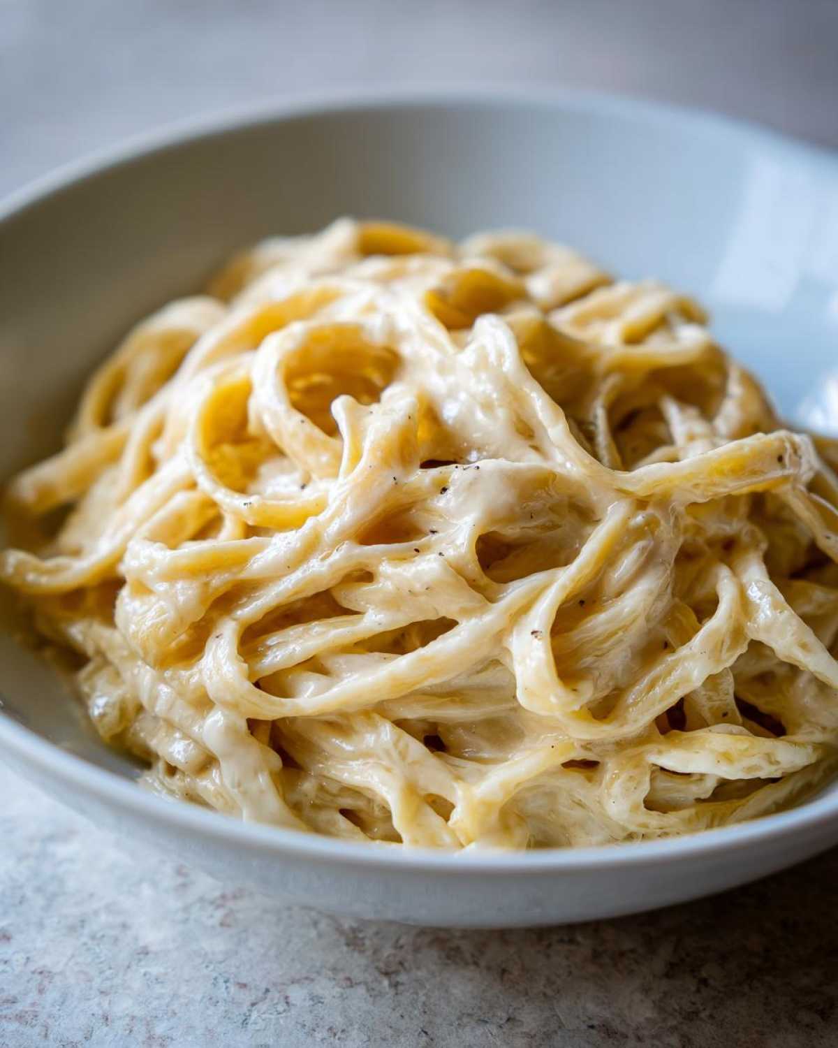 Close-up of fettuccine pasta coated in rich, creamy Olive Garden Alfredo Sauce in a light blue bowl.
