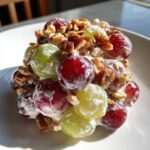 Close-up of a serving of creamy grape salad, featuring red and green grapes coated in dressing and topped with chopped pecans, similar to chicken salad chick grape salad.
