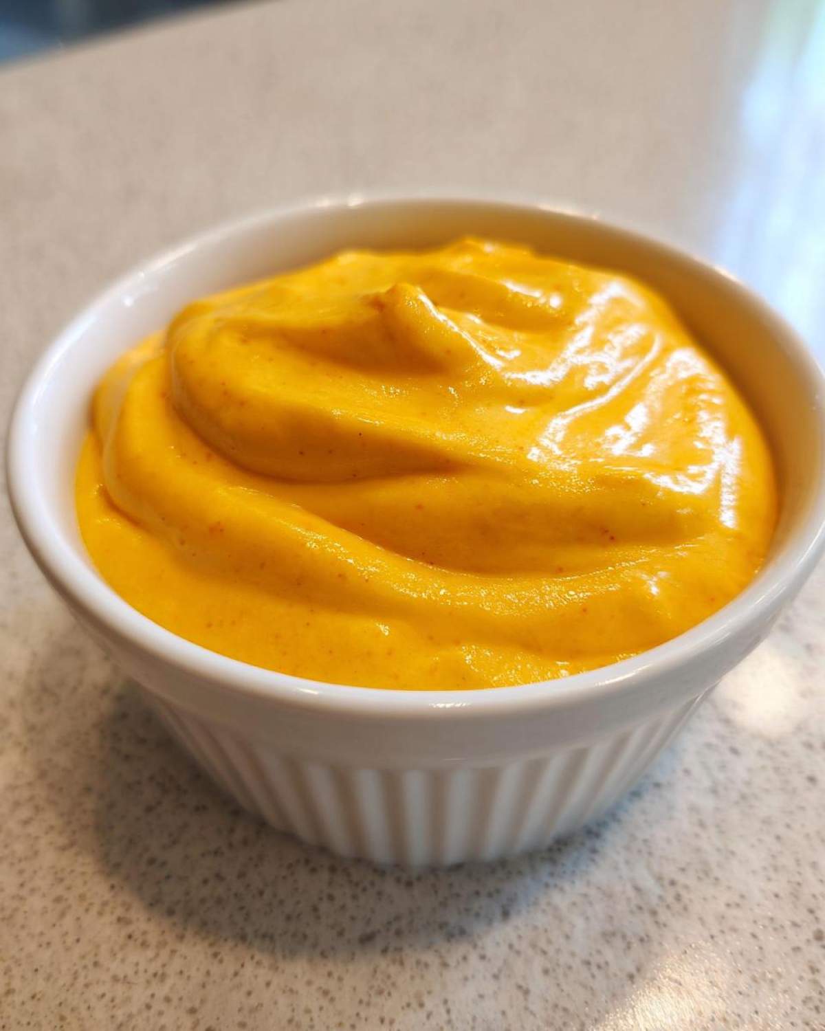 Close-up of rich, bright orange homemade nacho cheese sauce served in a small white fluted bowl.