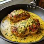 Two golden-brown chicken breasts smothered in a rich, creamy lemon chicken sauce dotted with fresh parsley.