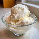 Close-up of two scoops of creamy, white protein ice cream served in a small clear glass bowl.