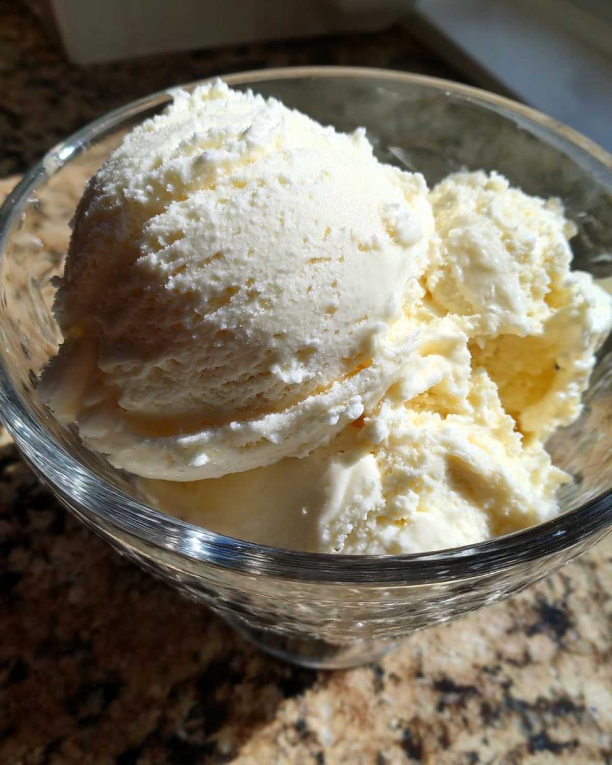 Close-up of creamy vanilla protein ice cream scoops in a clear glass bowl, glistening in the sun.