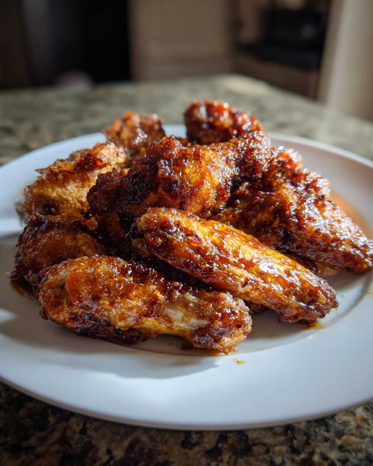 A close-up of several crispy, glazed chicken wings piled on a white plate, showcasing a rich, dark caramel coating.