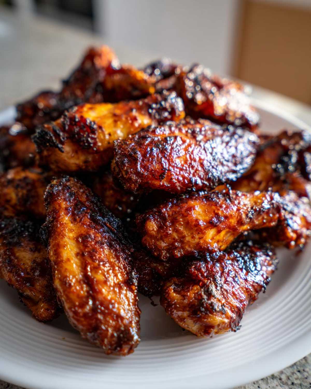 A close-up shot of a mound of perfectly cooked, crispy, and glazed chicken wings piled high on a white plate.