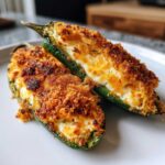 Two halves of baked jalapeño poppers filled with creamy cheese and topped with golden brown crispy breading.