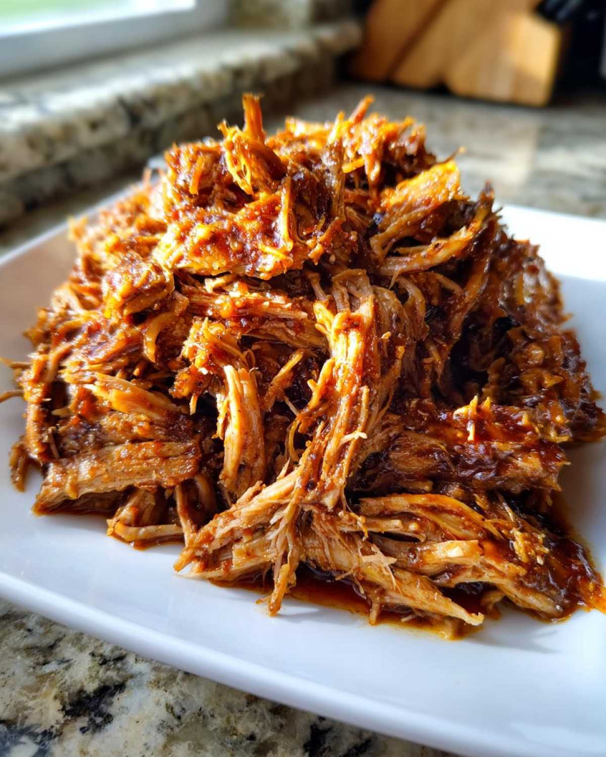 A close-up of tender, saucy crock pot pulled pork piled high on a white serving dish.