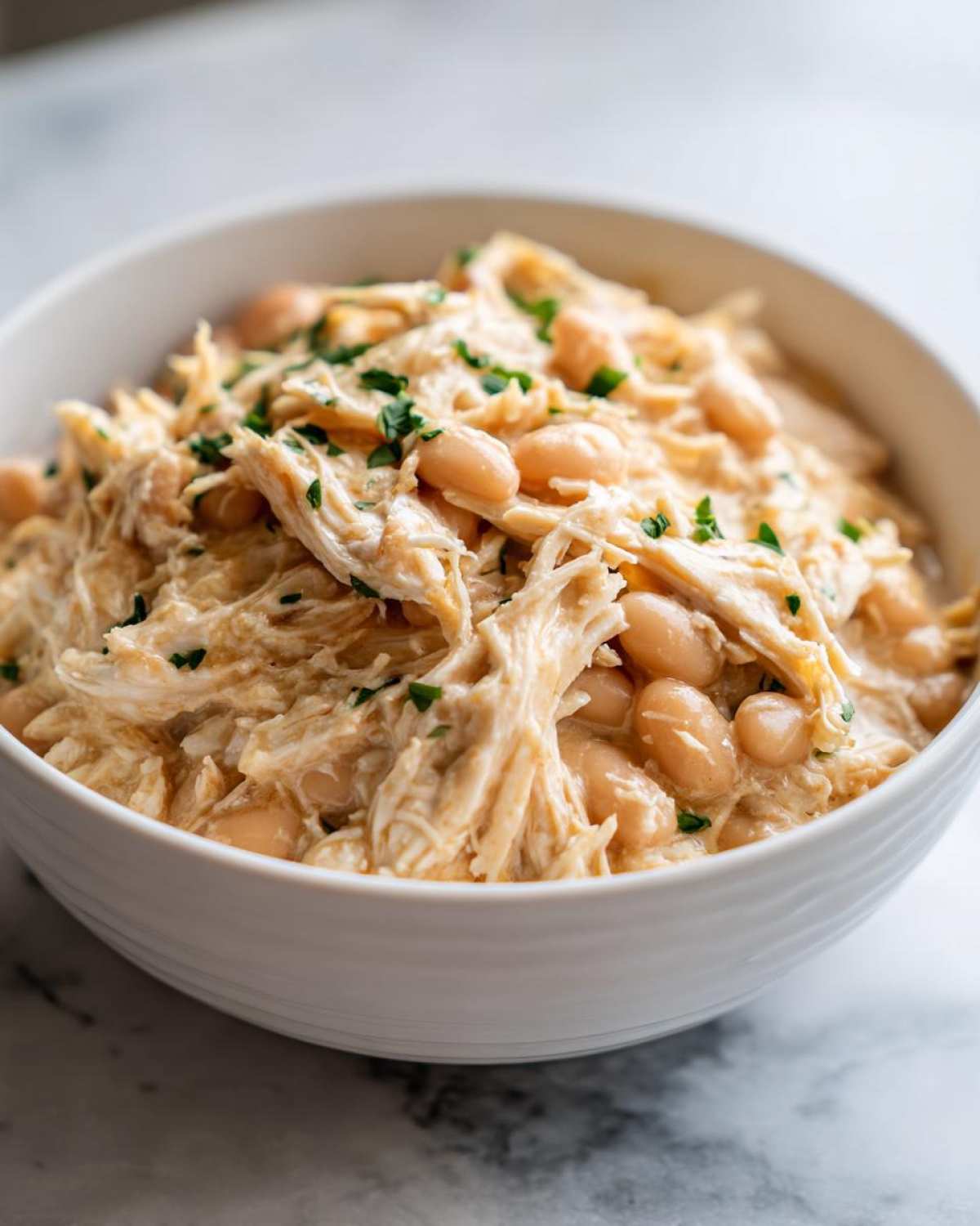 Close-up of a bowl filled with shredded chicken and white beans from the crockpot white chicken chili, garnished with parsley.