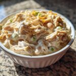 Close-up of a white bowl filled with creamy crockpot white chicken chili, showing shredded chicken, beans, and green onions.
