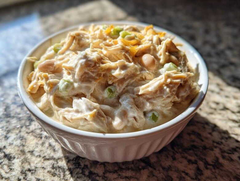 Close-up of a white bowl filled with creamy crockpot white chicken chili, showing shredded chicken, beans, and green onions.