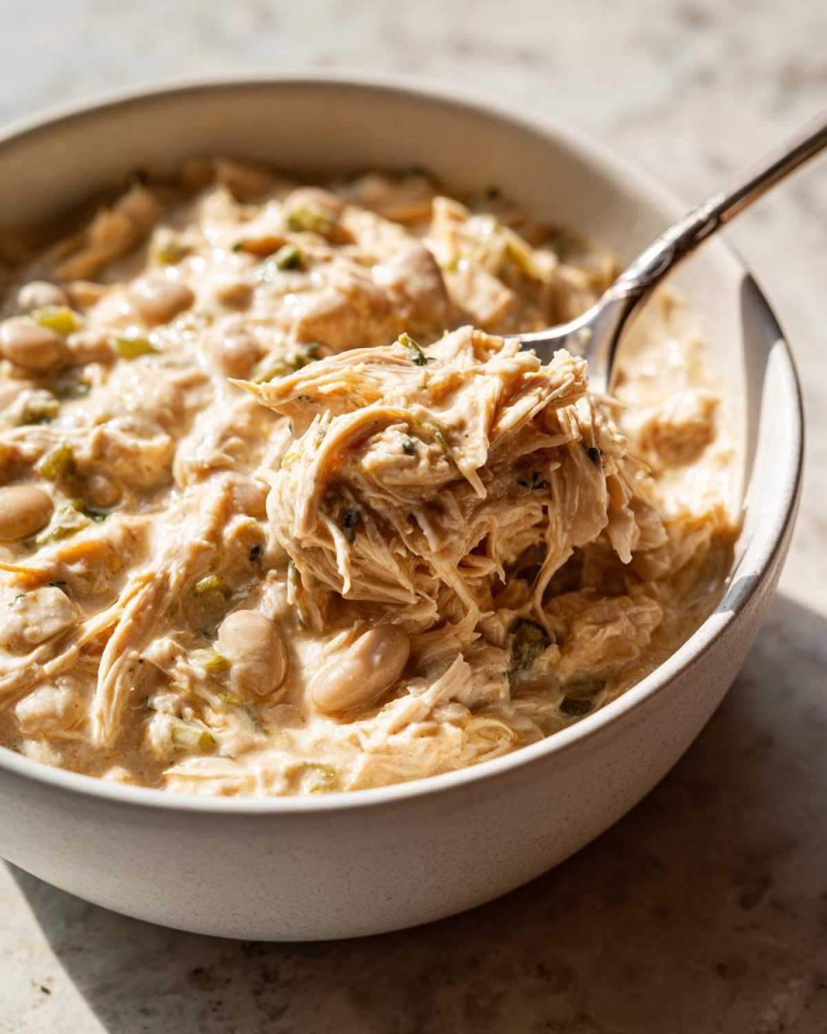 A spoonful of creamy crockpot white chicken chili showing shredded chicken and white beans.