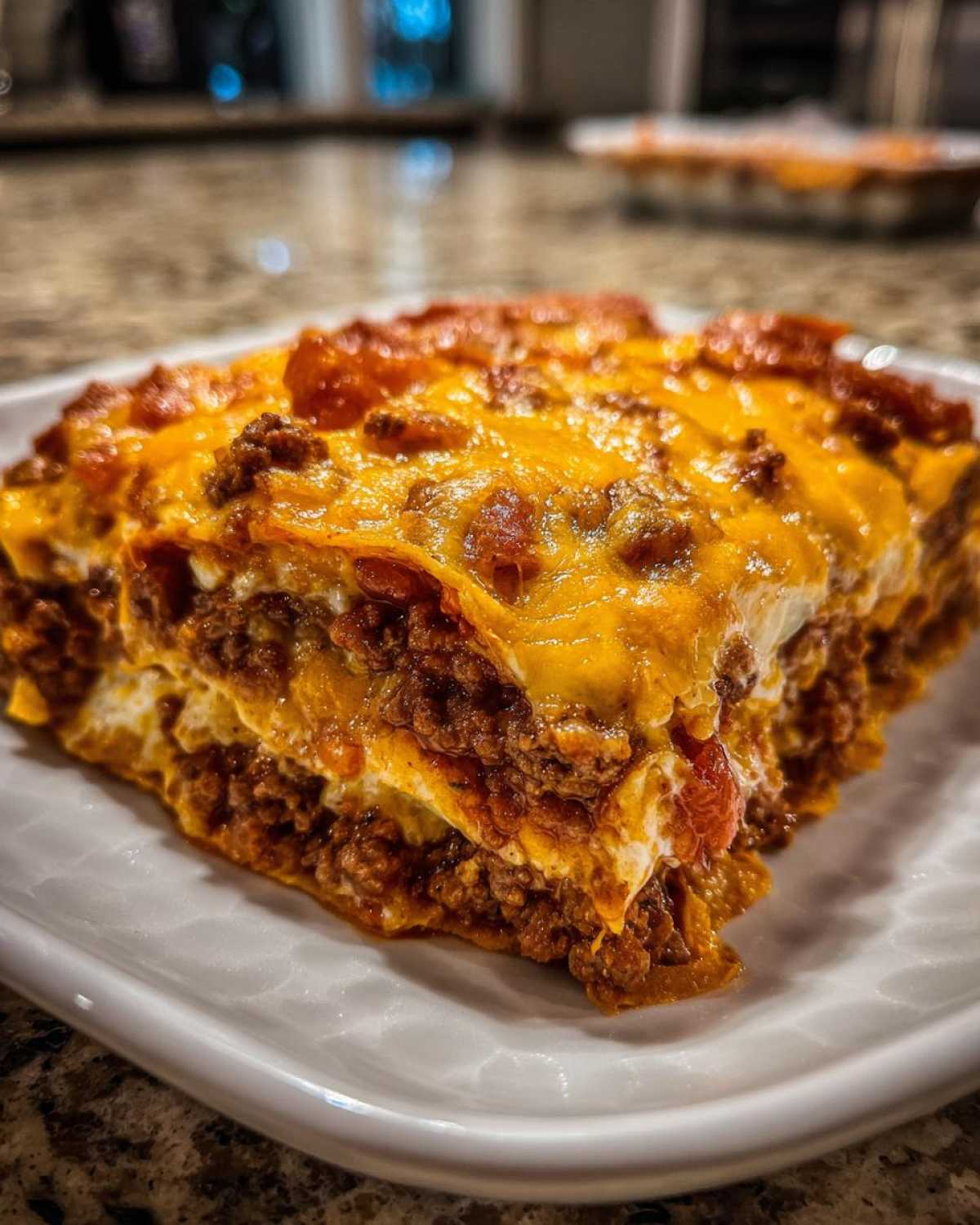 A close-up, mouth-watering slice of Dorito Casserole layered with seasoned beef and melted cheddar cheese.