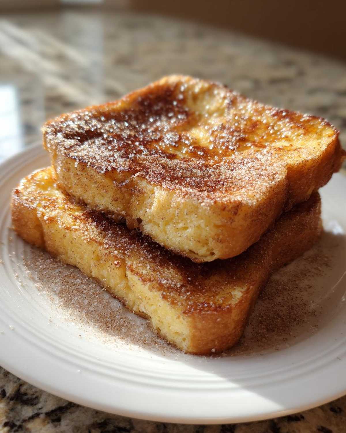 Two thick slices of easy French toast stacked, generously coated in cinnamon sugar, on a white plate.