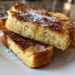 Close-up of thick, golden brown easy french toast slices dusted with powdered sugar on a white plate.