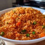 Close-up of a white bowl filled with vibrant orange spanish rice mixed with peas and carrots.