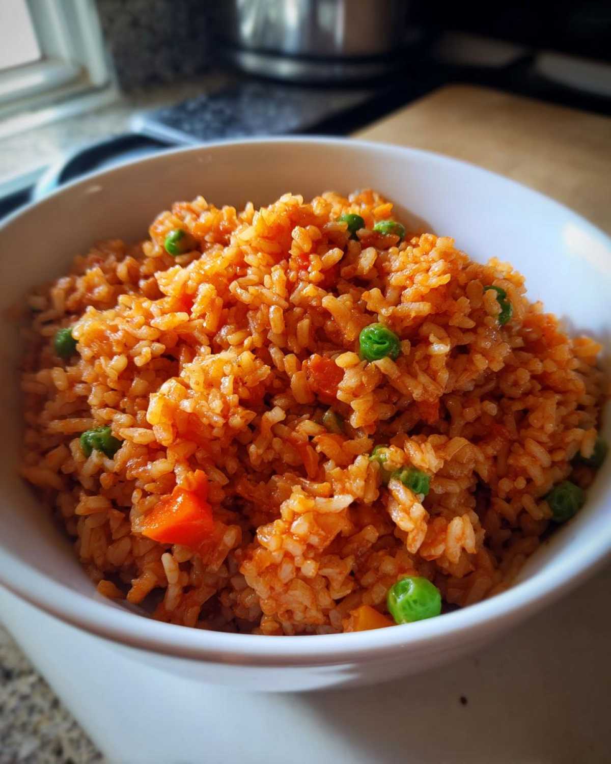 Close-up of a white bowl filled with bright orange spanish rice mixed with green peas and diced carrots.