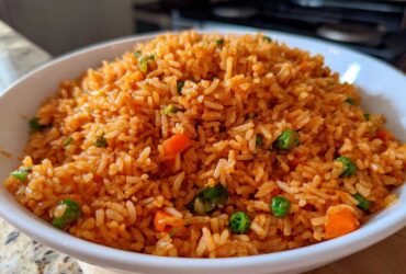 Close-up of a white bowl filled with vibrant orange spanish rice mixed with peas and carrots.