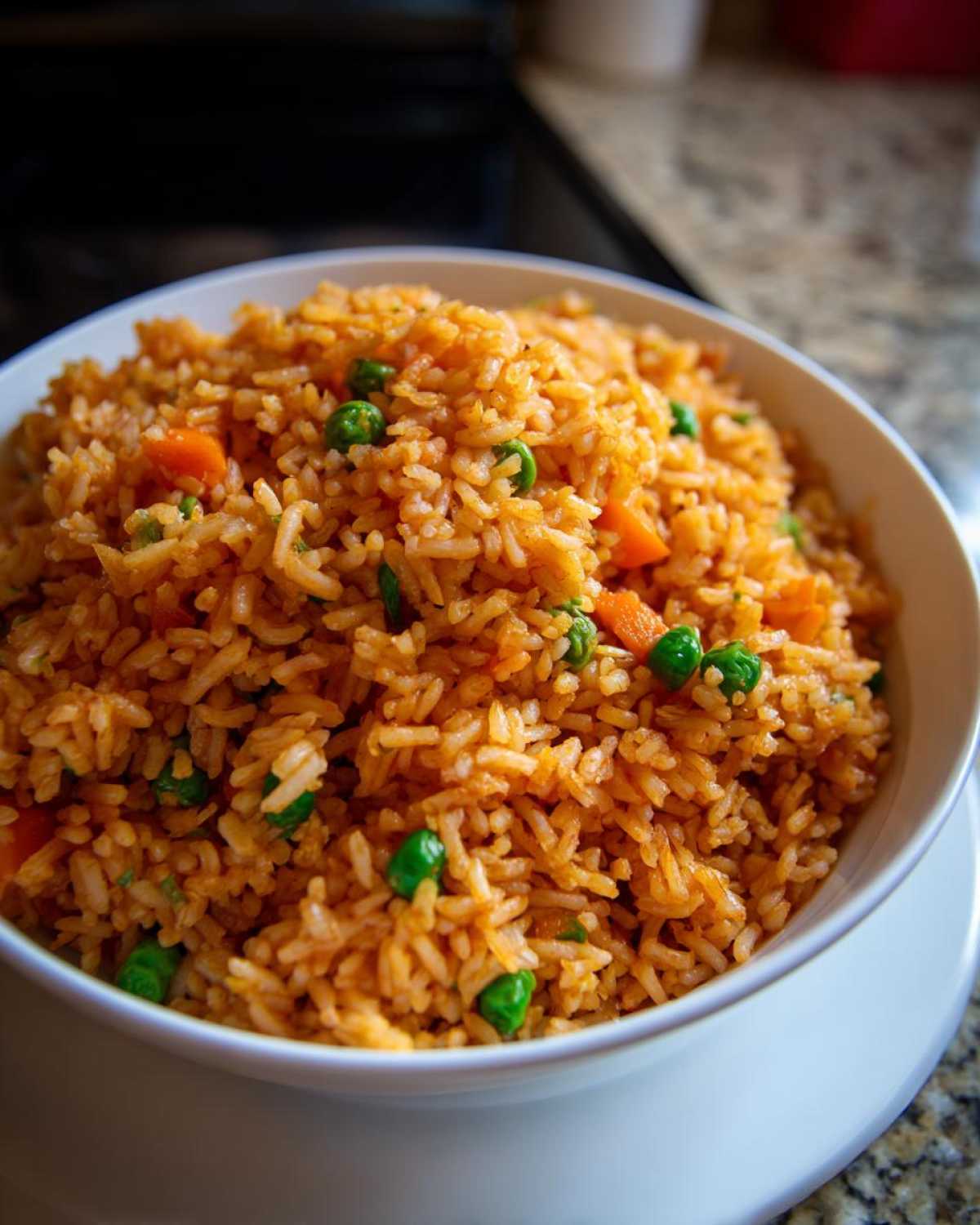 A close-up view of bright orange spanish rice mixed with green peas and diced carrots served in a white bowl.