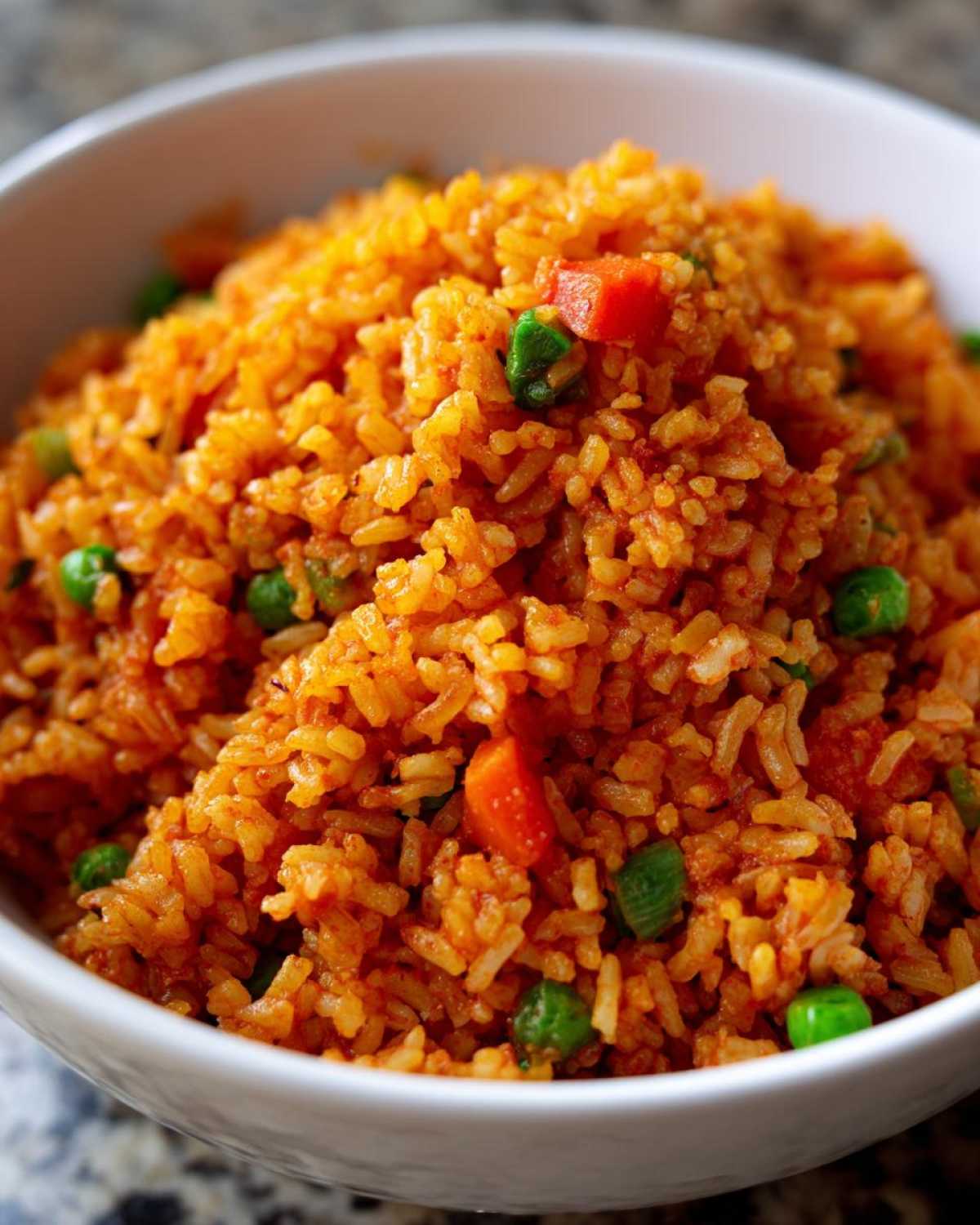 Close-up of vibrant orange spanish rice mixed with bright green peas and diced carrots in a white bowl.