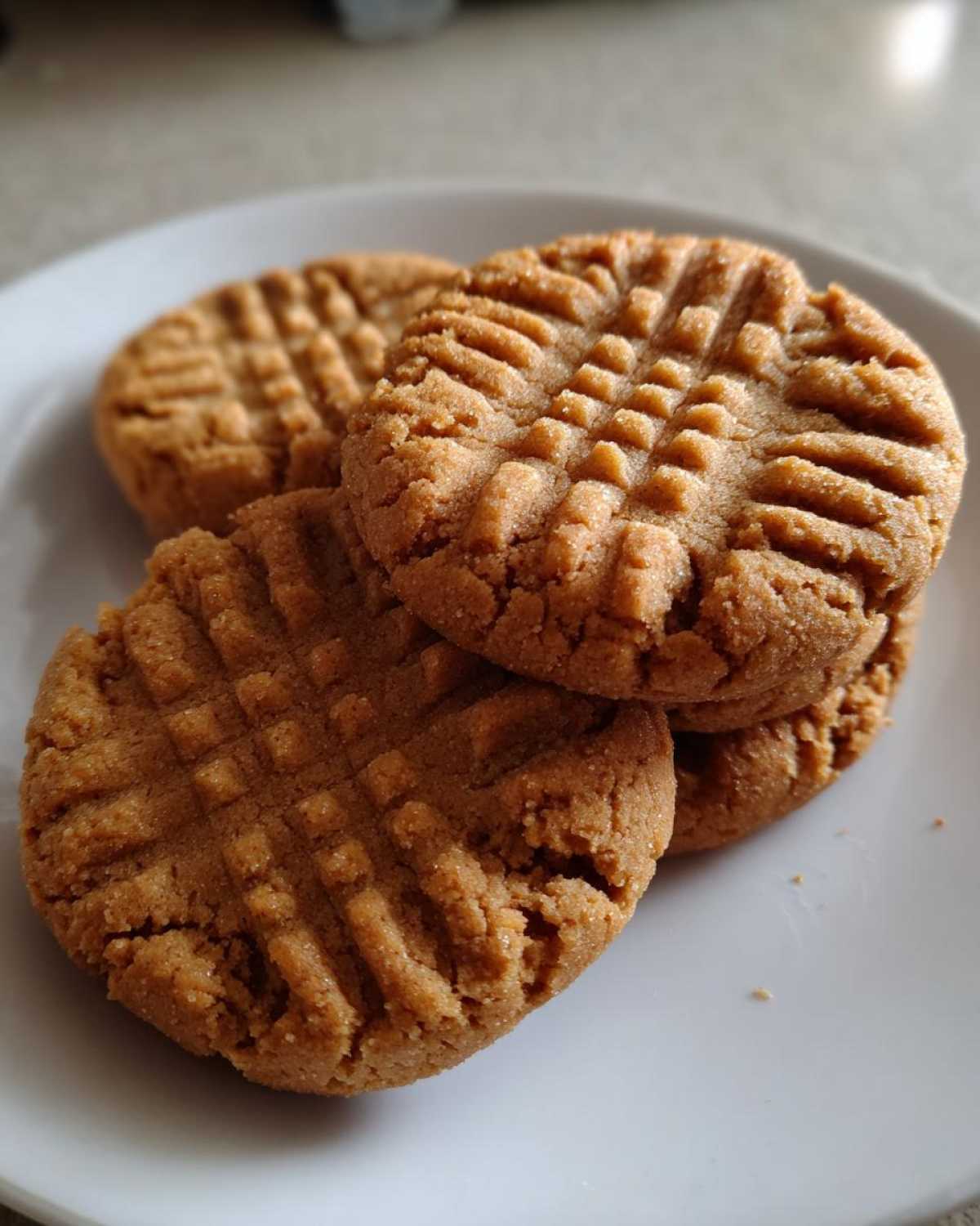 A stack of freshly baked Easy Peanut Butter Cookies showing the classic crisscross fork pattern on a white plate.
