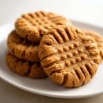 Close-up of several Easy Peanut Butter Cookies stacked on a white plate, showing classic crisscross fork marks.