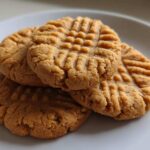 Close-up of a small stack of golden brown Easy Peanut Butter Cookies showing classic criss-cross fork marks on a white plate.