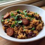 A white bowl filled with savory black beans and rice mixed with sliced sausage and topped with fresh cilantro.