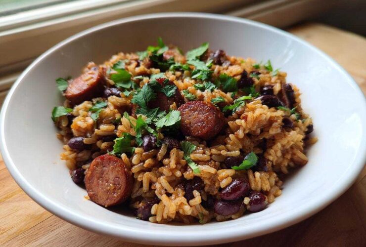 A white bowl filled with savory black beans and rice mixed with sliced sausage and topped with fresh cilantro.