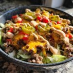 Close-up of a vibrant cheeseburger bowl featuring ground beef, melted cheddar cheese, jalapeños, and special sauce over lettuce.